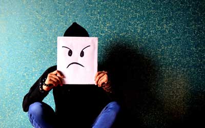 Sitting man with angry face drawing held up in front of his face