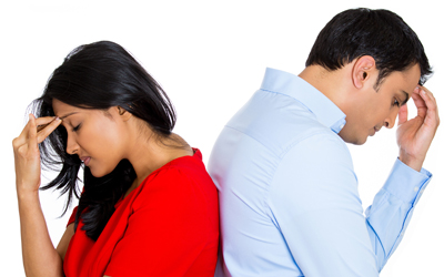 South Asian couple standing back to back with their hands on their foreheads in frustration